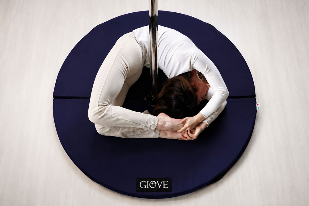 Atleta esegue una figura di flessibilità su palo da pole dance protetta dal Crash Mat Giove blu.